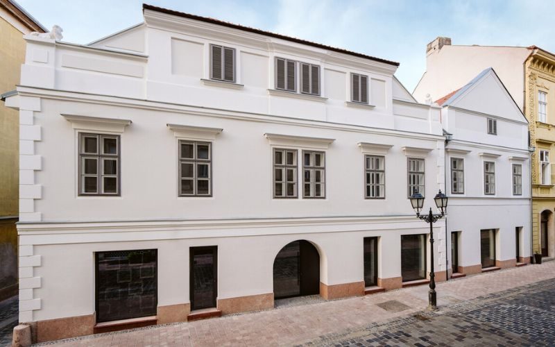 Felújított, klasszicista homlokzatú belvárosi épület macskaköves utcán, boltíves kapualjjal