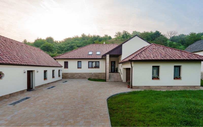 A teljes udvar a domboldal előtt: az L alakú ház két szárnya és a térkövezett beálló.